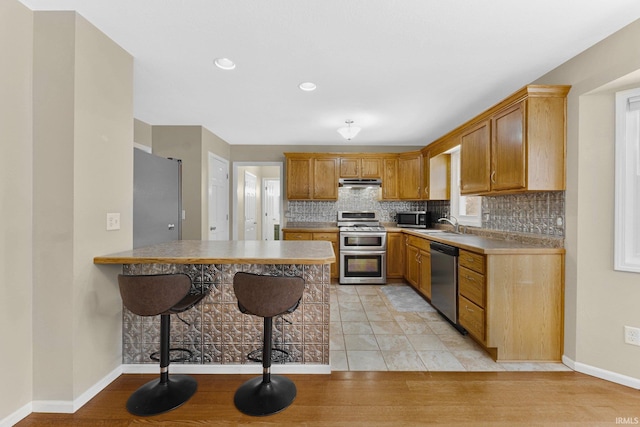 kitchen with kitchen peninsula, a kitchen bar, sink, light tile patterned flooring, and stainless steel appliances