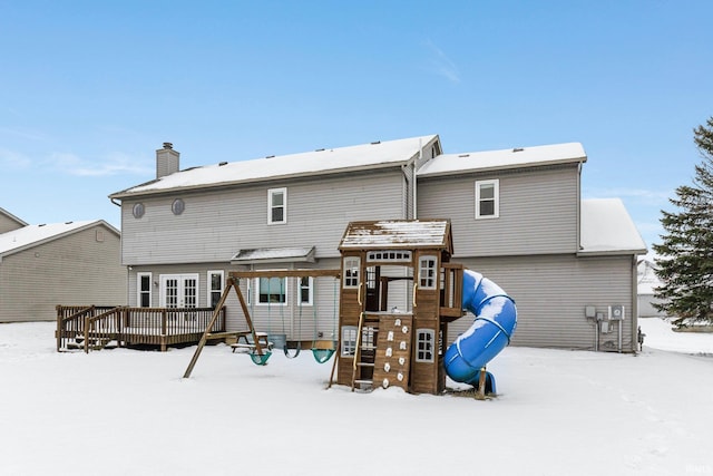 snow covered house with a playground and a deck