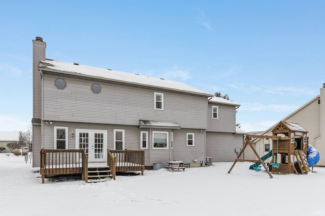 snow covered back of property featuring central air condition unit, a wooden deck, and a playground