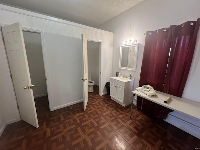 bathroom featuring toilet, parquet flooring, vanity, and a textured ceiling