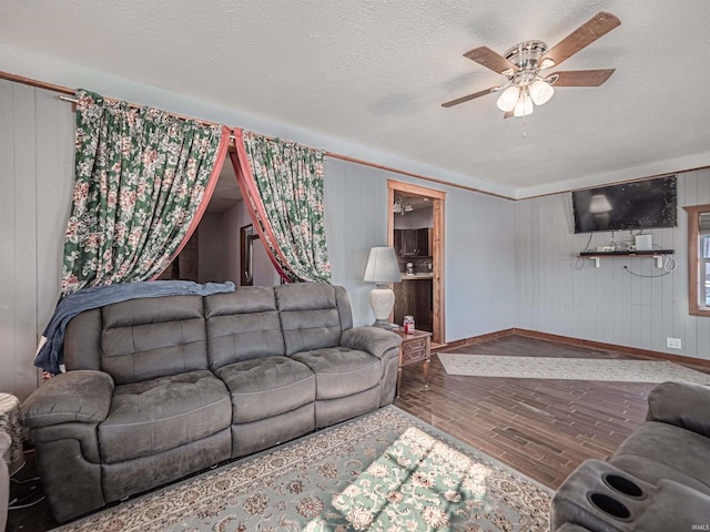 living room with ceiling fan, wood walls, a textured ceiling, and hardwood / wood-style flooring