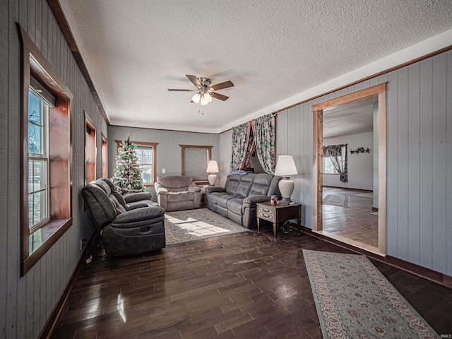 living room with ceiling fan, a textured ceiling, and wood walls