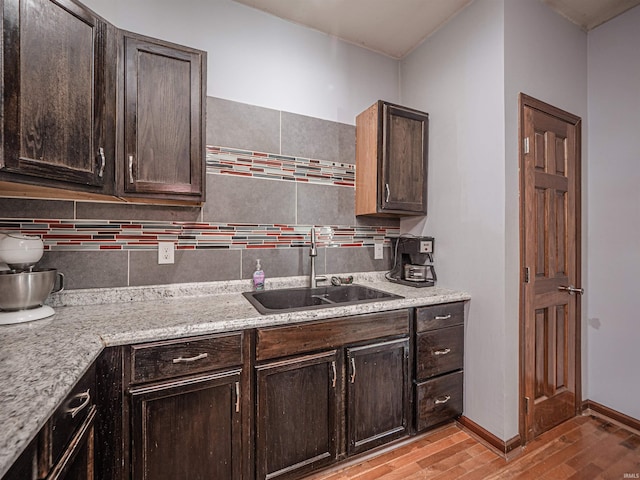 kitchen featuring dark brown cabinetry, tasteful backsplash, light hardwood / wood-style floors, sink, and light stone counters