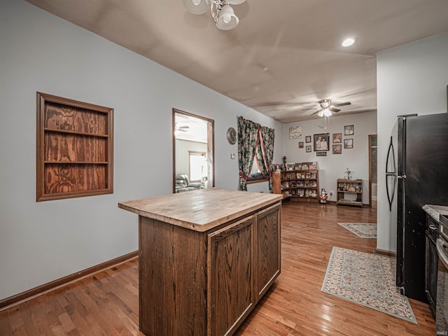 kitchen featuring butcher block countertops, ceiling fan, black fridge, light wood-type flooring, and a center island