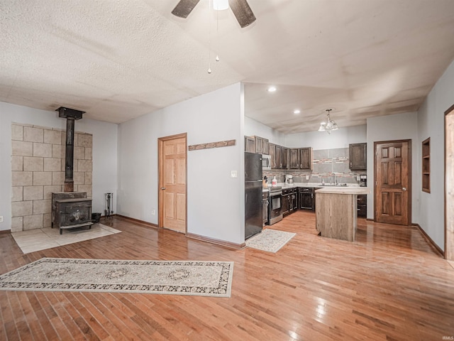 unfurnished living room with ceiling fan, sink, light wood-type flooring, a wood stove, and a textured ceiling