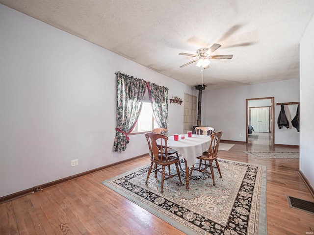 dining space featuring ceiling fan, hardwood / wood-style floors, a wood stove, and a textured ceiling