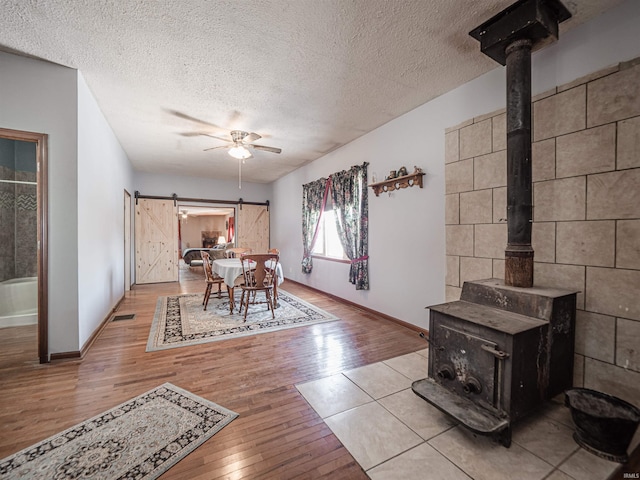 dining space featuring ceiling fan, a wood stove, a textured ceiling, and a barn door