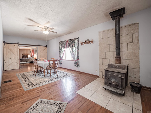 dining room with ceiling fan, a wood stove, a textured ceiling, and a barn door