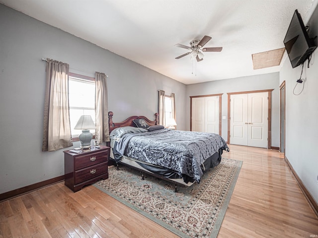 bedroom featuring ceiling fan, light wood-type flooring, and multiple closets