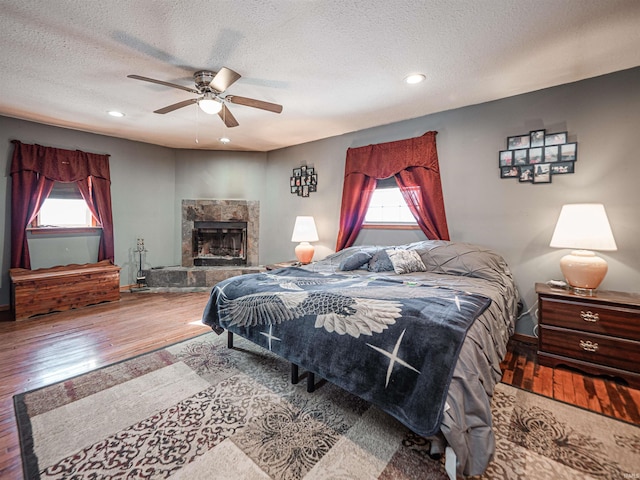 bedroom with ceiling fan, a fireplace, a textured ceiling, and hardwood / wood-style floors