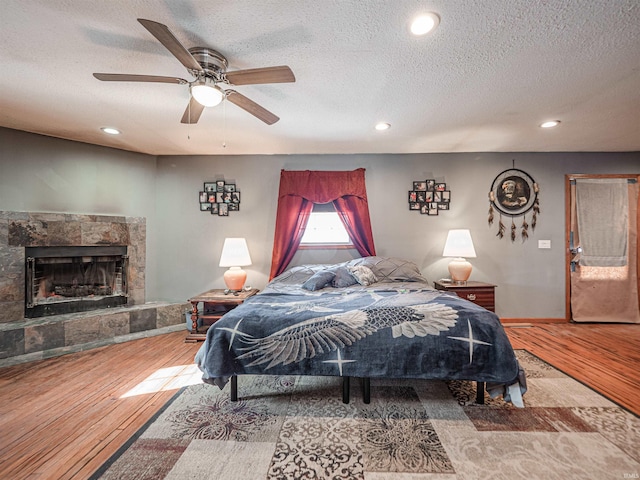 bedroom with ceiling fan, a stone fireplace, a textured ceiling, and hardwood / wood-style flooring