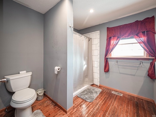 bathroom with toilet, a shower with shower curtain, a textured ceiling, and hardwood / wood-style flooring