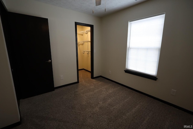 unfurnished bedroom featuring a spacious closet, ceiling fan, carpet, a closet, and a textured ceiling