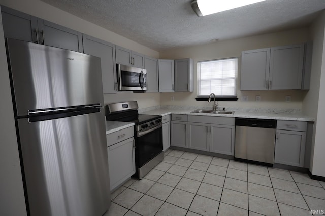 kitchen featuring a textured ceiling, stainless steel appliances, sink, light tile patterned floors, and gray cabinetry