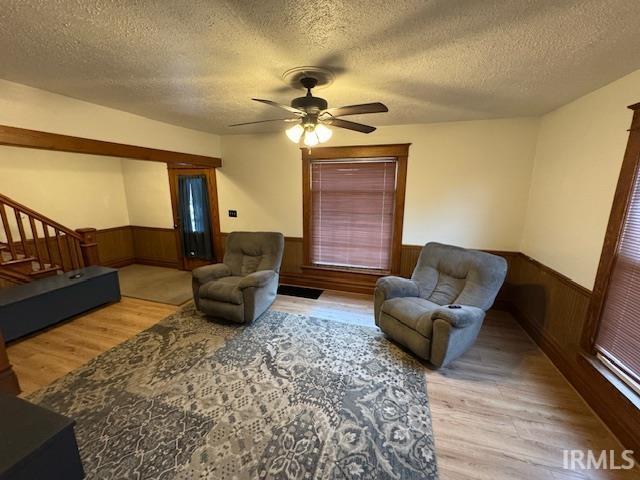 living room featuring ceiling fan, light wood-type flooring, wooden walls, and a textured ceiling