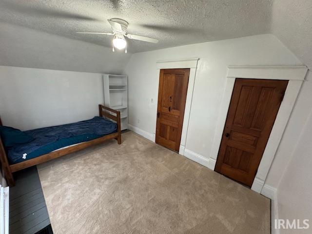 unfurnished bedroom with ceiling fan, carpet flooring, a textured ceiling, and lofted ceiling