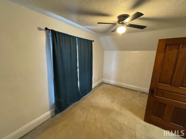 bonus room featuring ceiling fan, light colored carpet, vaulted ceiling, and a textured ceiling