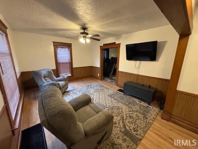 living room with ceiling fan, a textured ceiling, and light wood-type flooring