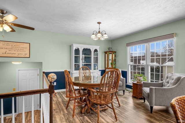 dining room featuring wood-type flooring, ceiling fan with notable chandelier, and a textured ceiling