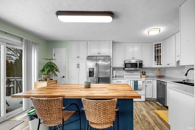 kitchen with wood counters, appliances with stainless steel finishes, white cabinetry, and sink