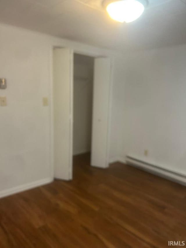 unfurnished bedroom featuring dark wood-type flooring, a baseboard radiator, and a closet