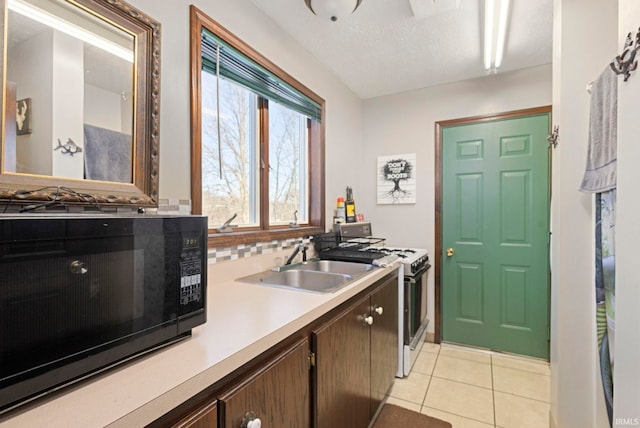 kitchen featuring white gas range oven, light tile patterned flooring, a textured ceiling, dark brown cabinetry, and sink