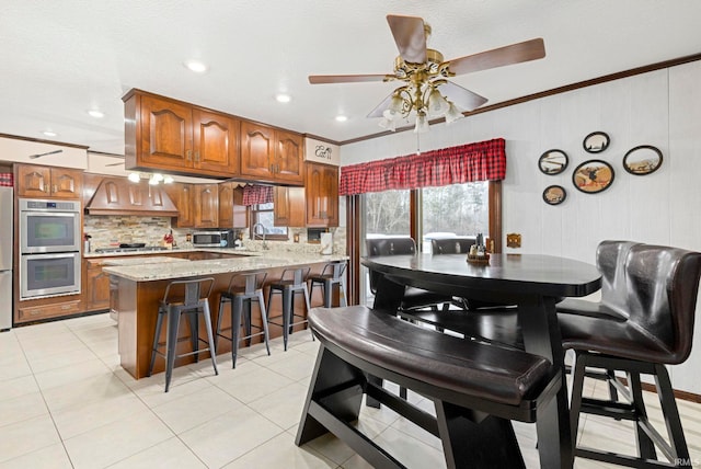 kitchen with ceiling fan, appliances with stainless steel finishes, a breakfast bar area, light stone countertops, and ornamental molding