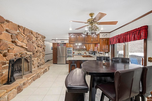 dining room with ceiling fan, light tile patterned floors, ornamental molding, and a fireplace