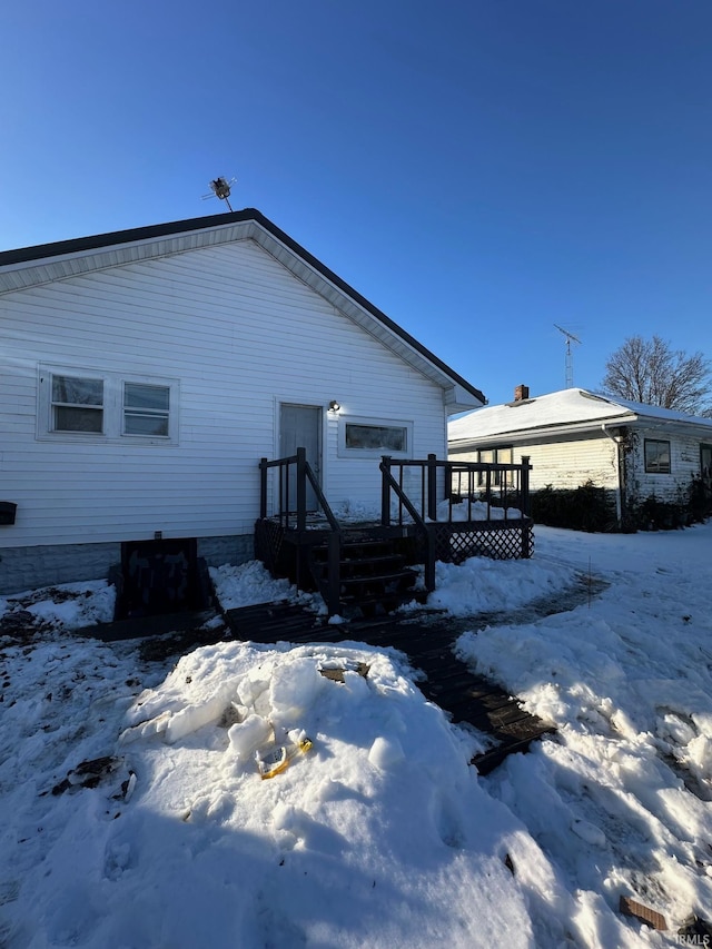 snow covered back of property with a wooden deck