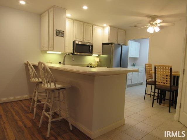 kitchen with a kitchen bar, kitchen peninsula, white cabinetry, and stainless steel appliances