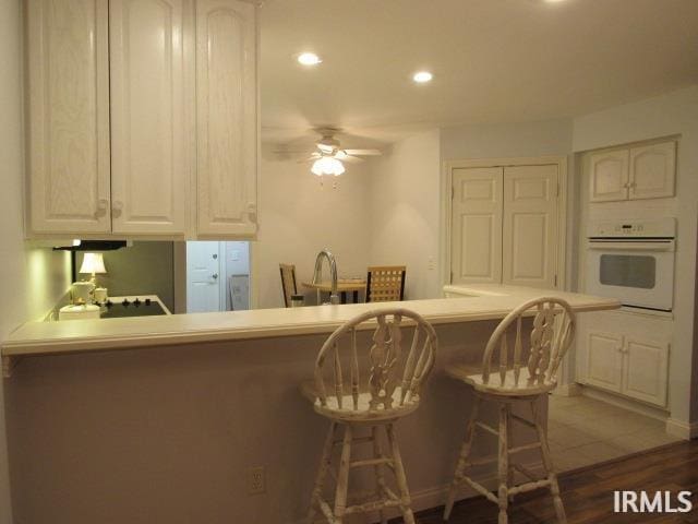 kitchen with white oven, kitchen peninsula, ceiling fan, dark hardwood / wood-style flooring, and a breakfast bar