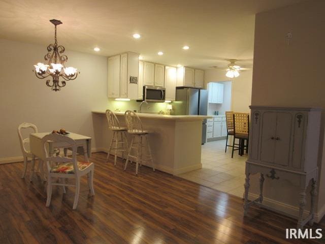 kitchen with a breakfast bar, kitchen peninsula, white cabinetry, hardwood / wood-style flooring, and stainless steel appliances