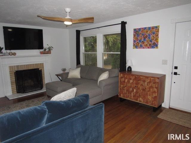 living room with a brick fireplace, a textured ceiling, dark hardwood / wood-style floors, and ceiling fan