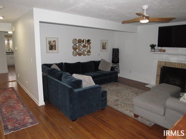 living room with a textured ceiling, ceiling fan, dark hardwood / wood-style floors, and a brick fireplace