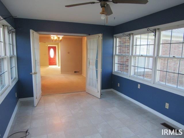 spare room featuring ceiling fan with notable chandelier