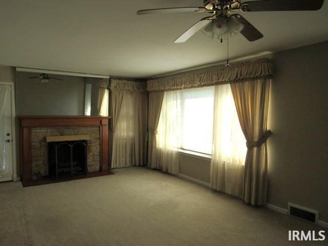 unfurnished living room with ceiling fan, carpet flooring, and a stone fireplace