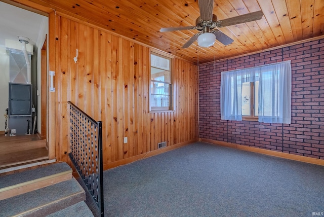 unfurnished room featuring ceiling fan, brick wall, wood ceiling, and carpet