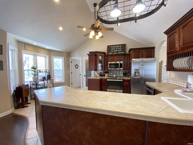 kitchen with appliances with stainless steel finishes, tile counters, sink, kitchen peninsula, and vaulted ceiling