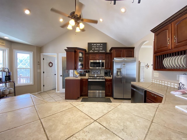 kitchen with ceiling fan, vaulted ceiling, appliances with stainless steel finishes, tile counters, and light tile patterned floors