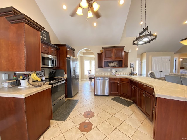 kitchen with light tile patterned floors, ceiling fan, stainless steel appliances, decorative light fixtures, and high vaulted ceiling