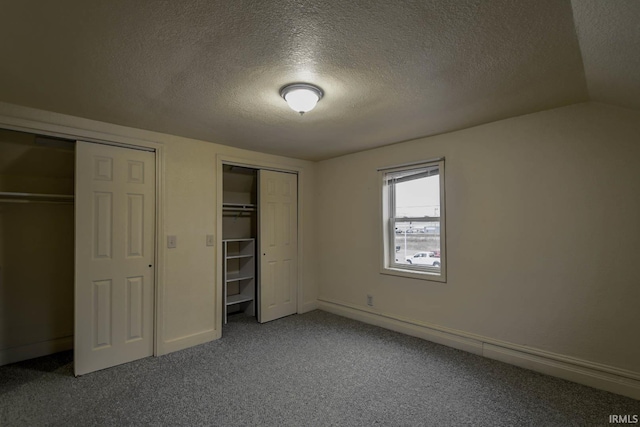 unfurnished bedroom with lofted ceiling, two closets, a textured ceiling, and carpet flooring