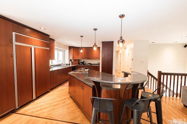 kitchen featuring decorative light fixtures, light wood-type flooring, paneled built in fridge, dark stone counters, and a kitchen island