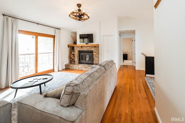 living room featuring vaulted ceiling, a stone fireplace, a chandelier, and hardwood / wood-style floors