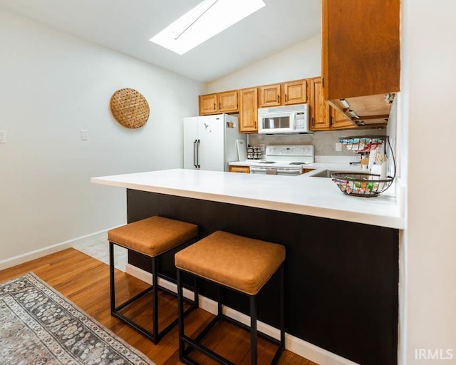 kitchen with a kitchen breakfast bar, lofted ceiling with skylight, kitchen peninsula, and white appliances