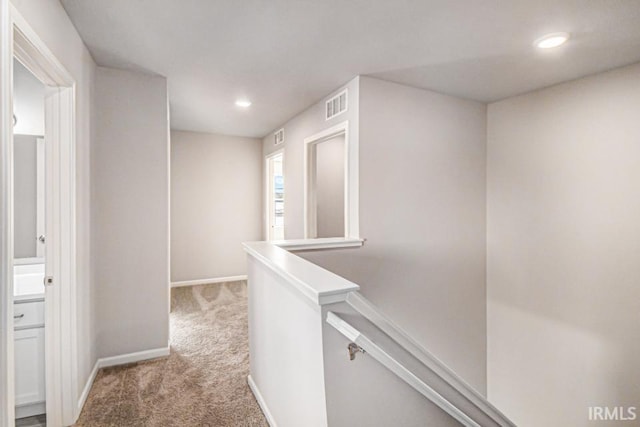 hallway with carpet floors, baseboards, visible vents, and an upstairs landing