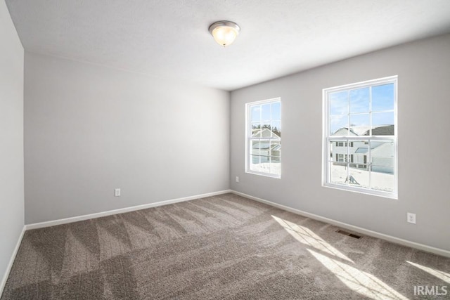 empty room with carpet, visible vents, and baseboards