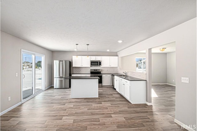 kitchen with wood finished floors, a sink, appliances with stainless steel finishes, backsplash, and dark countertops