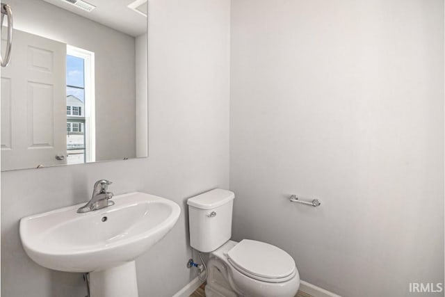 half bathroom featuring visible vents, a sink, toilet, and baseboards