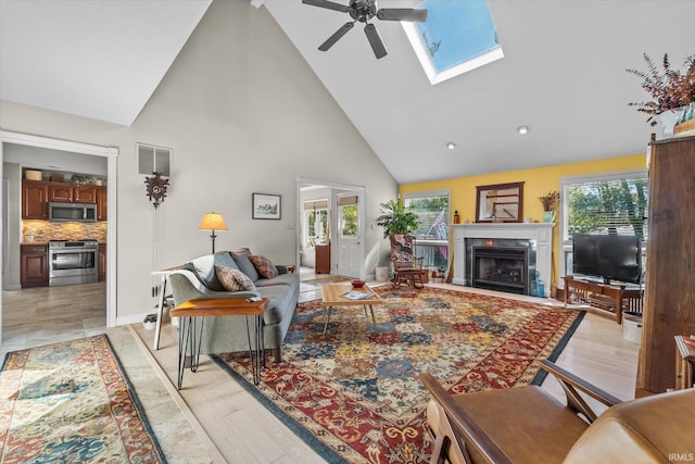 living room with high vaulted ceiling, a skylight, ceiling fan, and light wood-type flooring