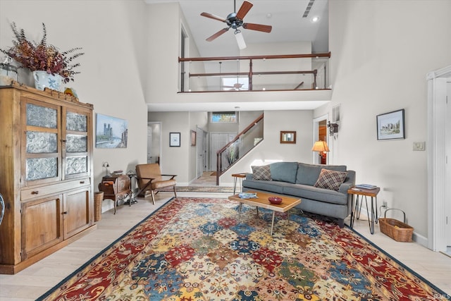 living room featuring ceiling fan, a towering ceiling, and light hardwood / wood-style floors